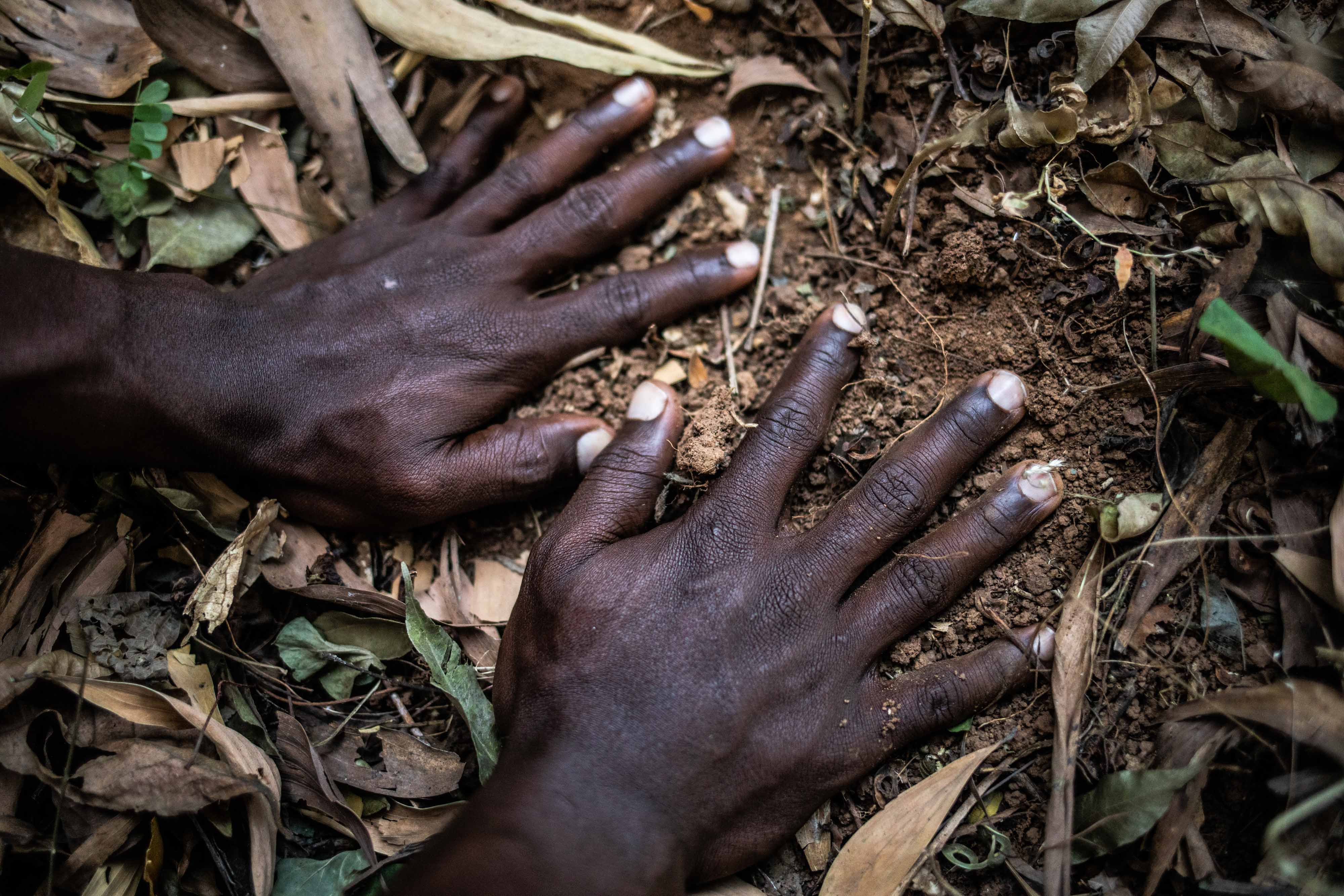 Telimele, Guinea. January 13, 2022. Lamarana, Abdoul’s brother, one of the passengers who died in Italy on January 23, 2019, <br>
touches the ground at the place where his brother was buried in his hometown. 
Abdoul’s body was repatriated to his country and rests in the cemetery of Telimele, a few meters from his home. ©︎ César Dezfuli